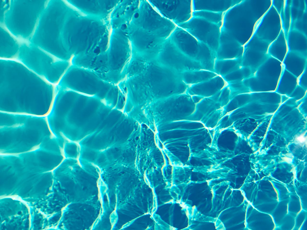 Bright turquoise water surface in sunlight, capturing shimmering patterns and reflections.